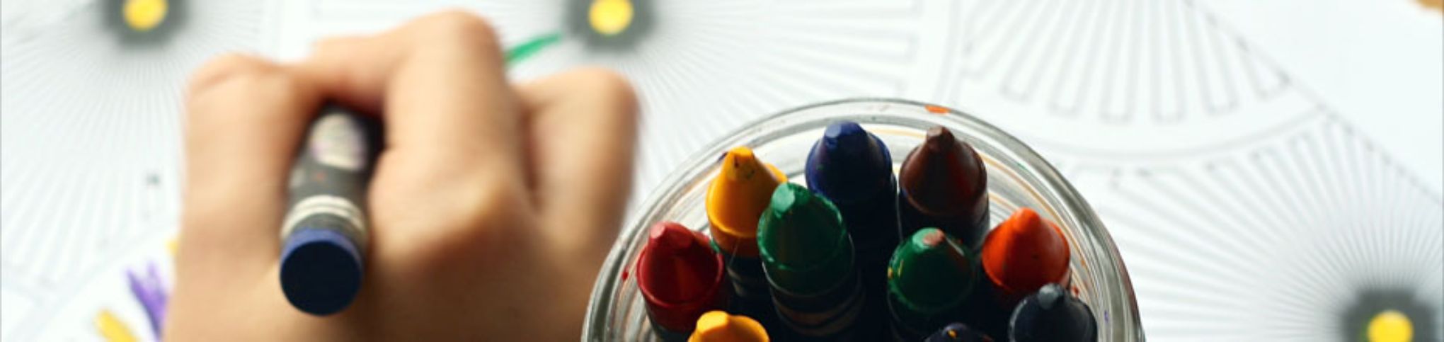 Imagen de un bote con ceras de colores y una mano pintando