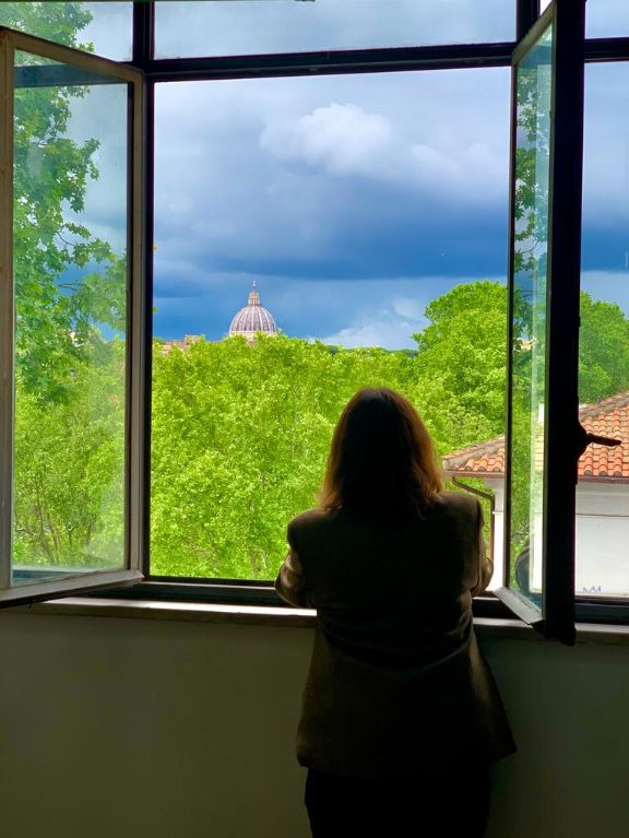 Profesora mirando por la ventana de un aula. Al fondo cúpula del Vaticano.