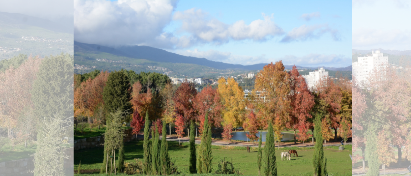 Campus universitario en otoño con árboles en tonos rojos y dorados, caballos pastando en pradera verde, estanque, edificios al fondo y montañas bajo c